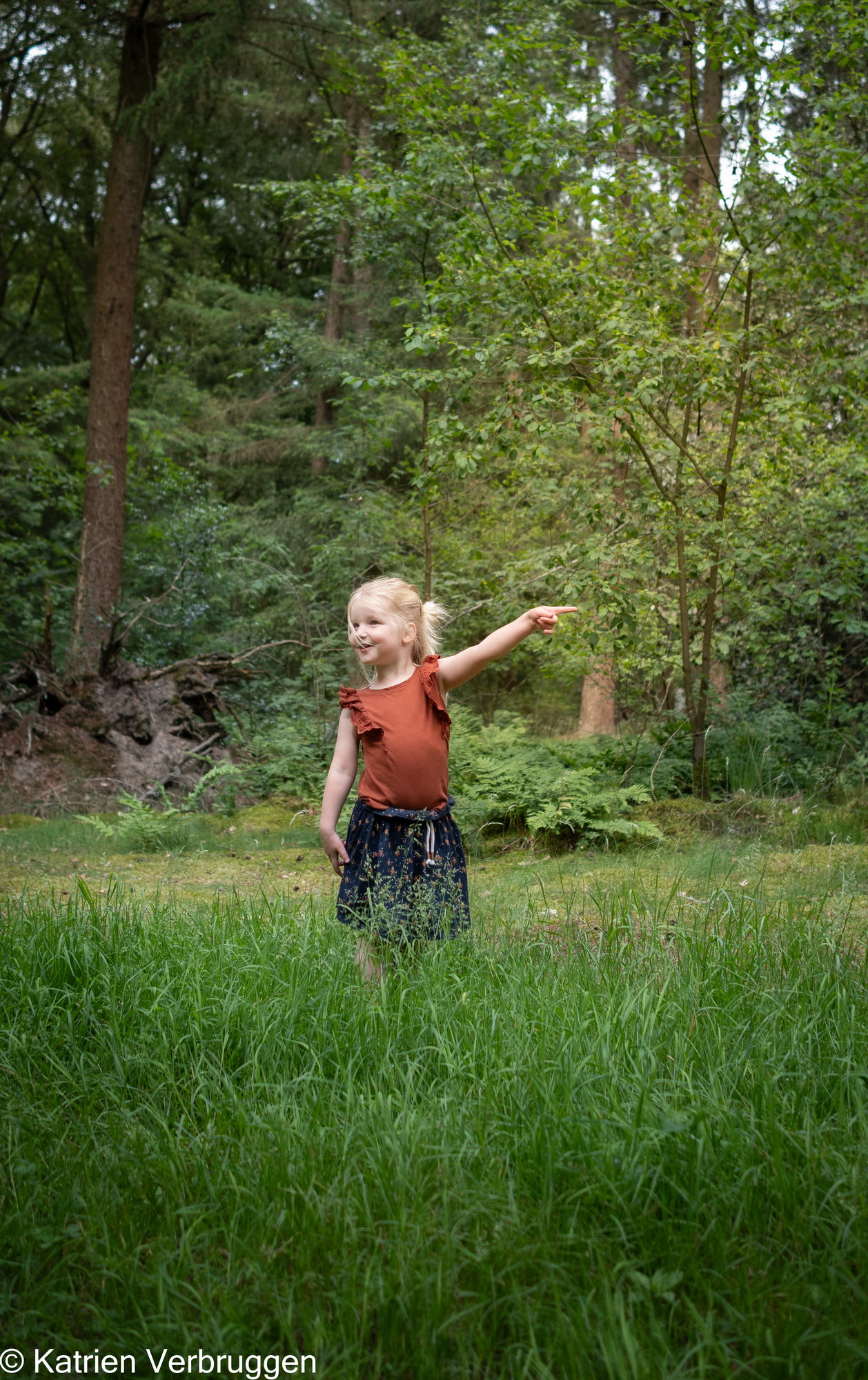 Meisje wijst iets aan in het hoge gras