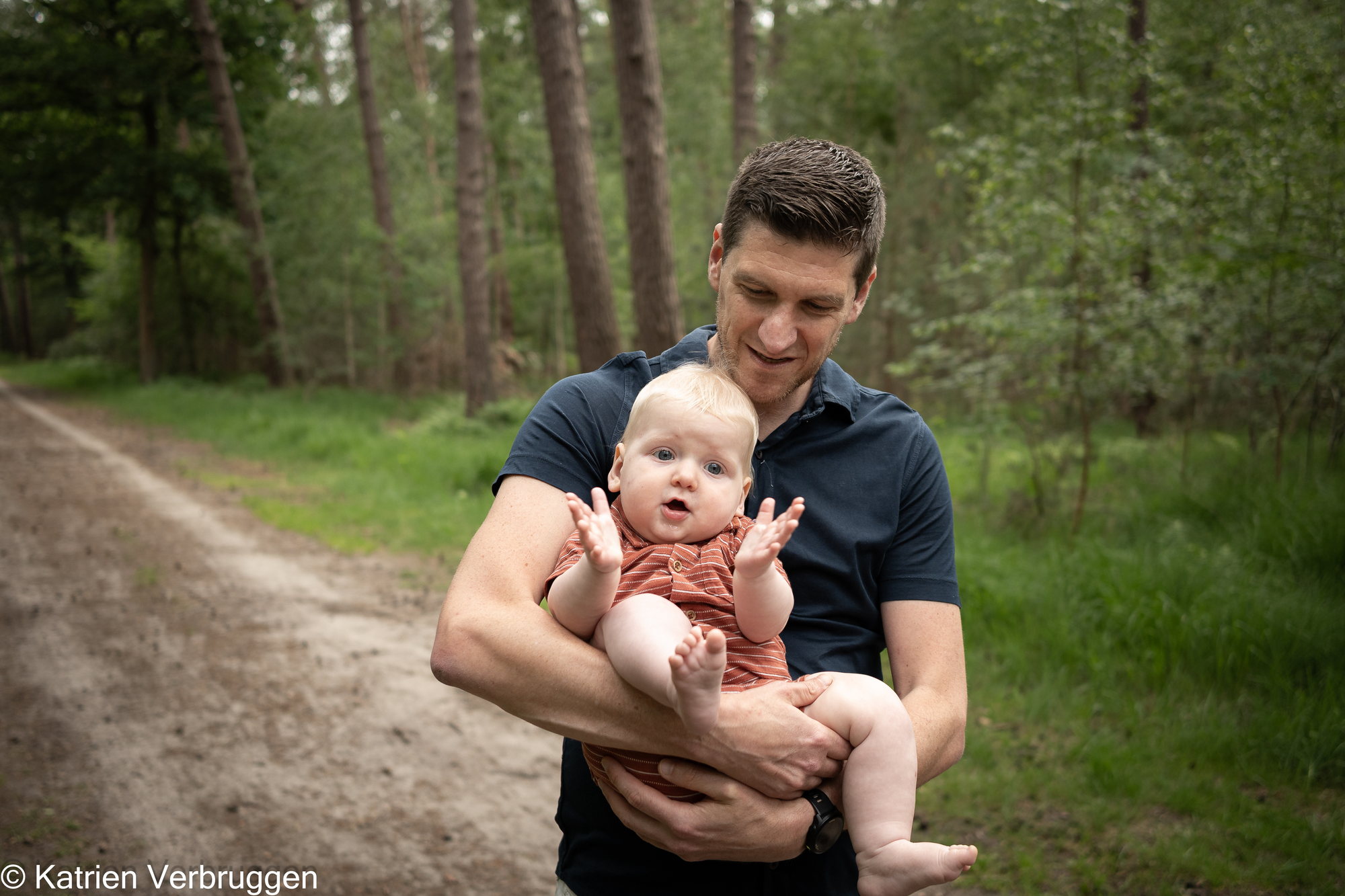 Papa draagt zijn baby over een bospad