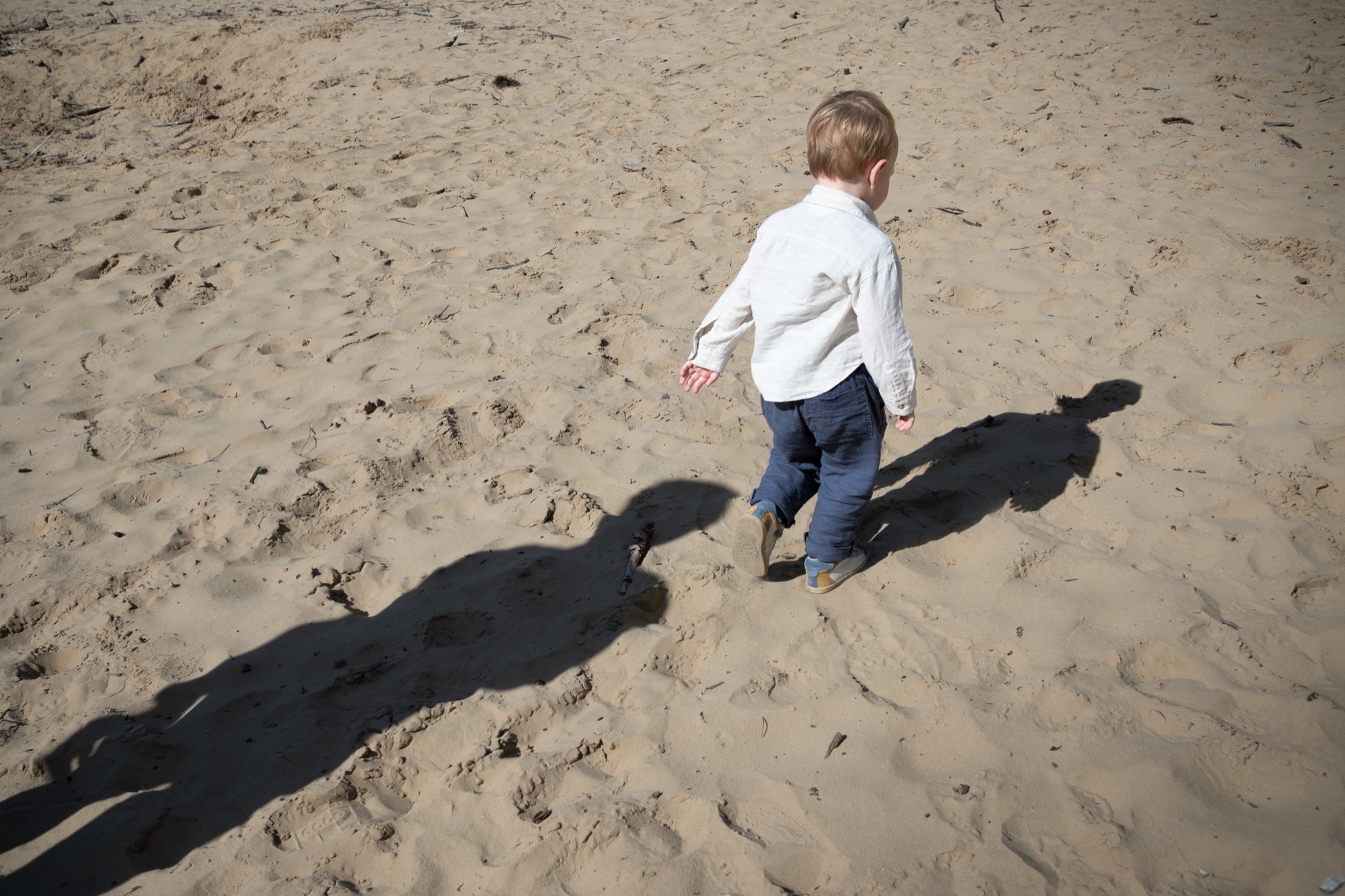Jongetje stapt door het zand, met de schaduwen van zijn ouders
